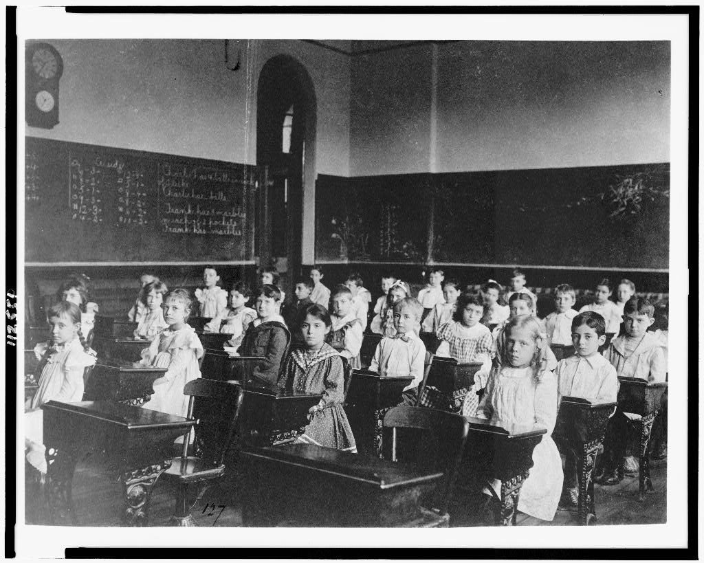 Estudiantes sentados en filas de pupitres en un aula de Washington, D.C., hacia 1899.